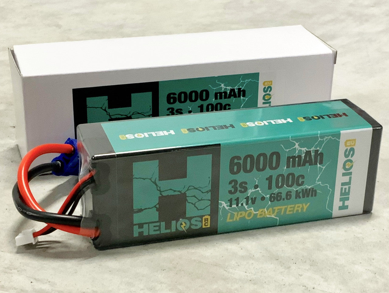 A 3S 6000 mAh 100C Lipo battery with wires, placed next to its white box packaging labeled '6000 mAh 3S 11.1V HeliOS'.
