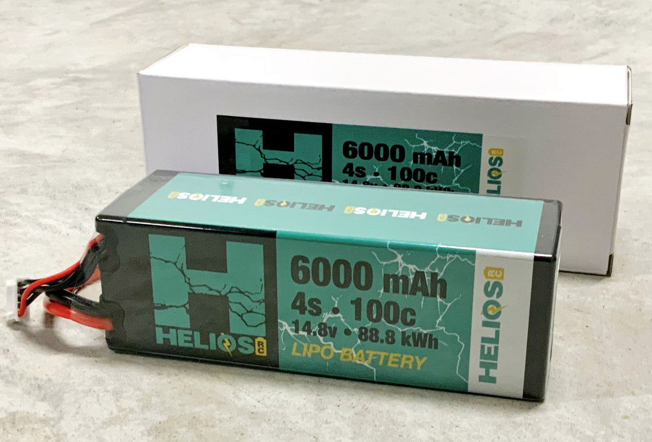 one 4S lithium polymer batteries with a capacity of 6000 mAh and 100C discharge rate, placed next to its packaging boxes. One battery is labeled with '6000 mAh' and the other with '100C' indicating the capacity and discharge specifics.