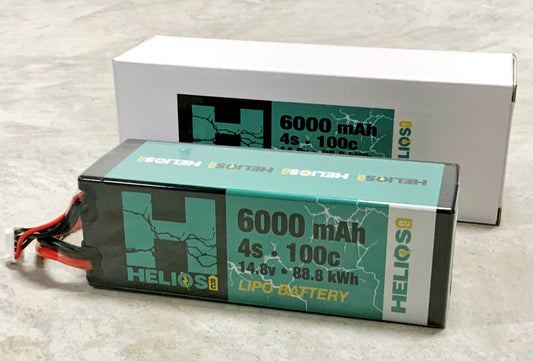 one 4S lithium polymer batteries with a capacity of 6000 mAh and 100C discharge rate, placed next to its packaging boxes. One battery is labeled with '6000 mAh' and the other with '100C' indicating the capacity and discharge specifics.